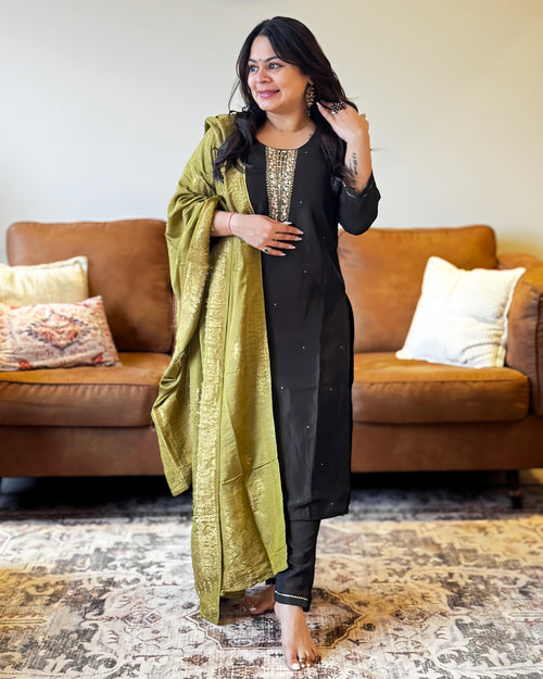 Woman in a black outfit with a green dupatta standing in a living room.