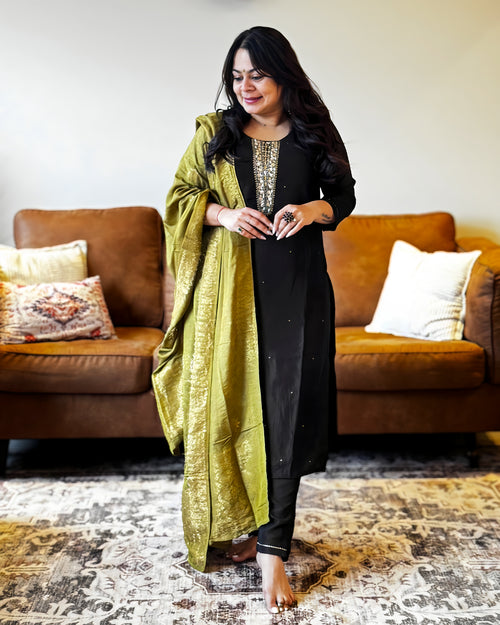 Woman in a black and green traditional outfit standing in a living room.
