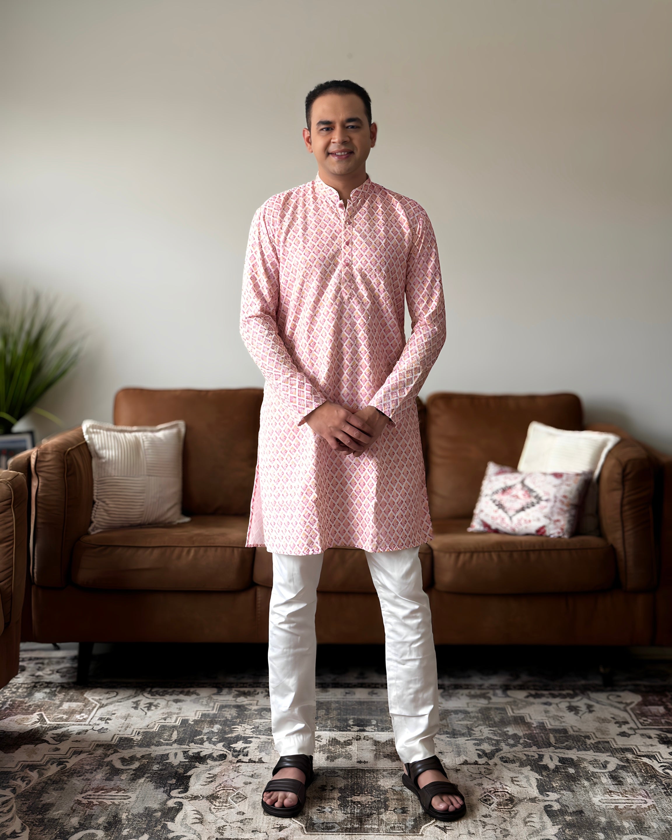 Man wearing a pink kurta with white pants standing in a living room.
