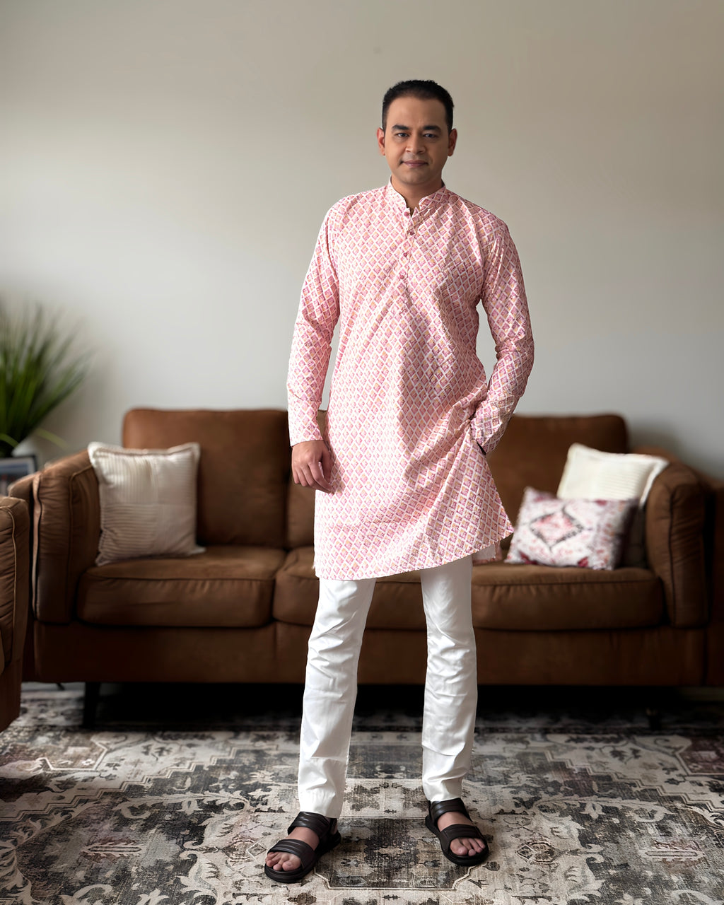 Man wearing a pink kurta with white pants standing in a living room.