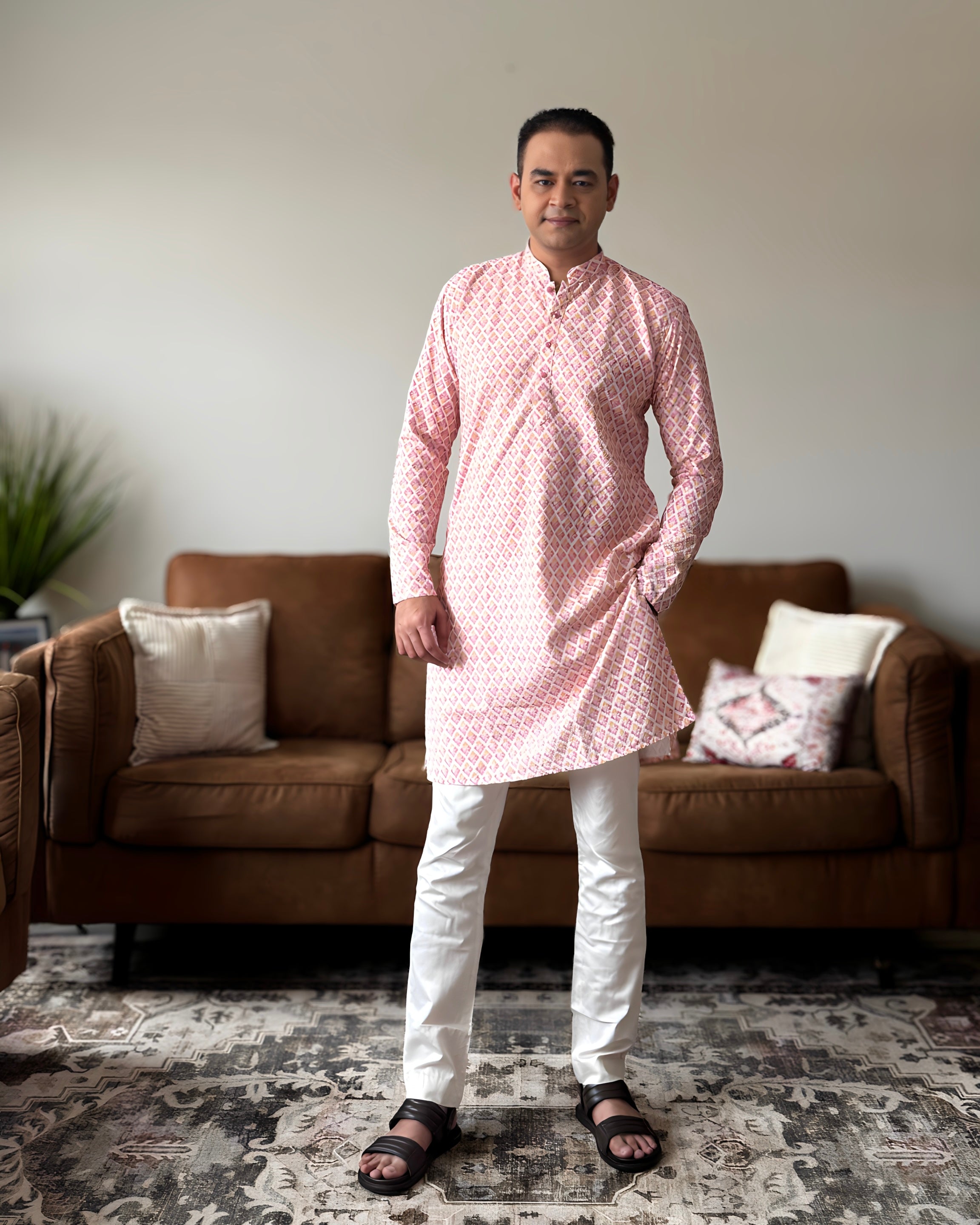 Man wearing a pink kurta with white pants standing in a living room.