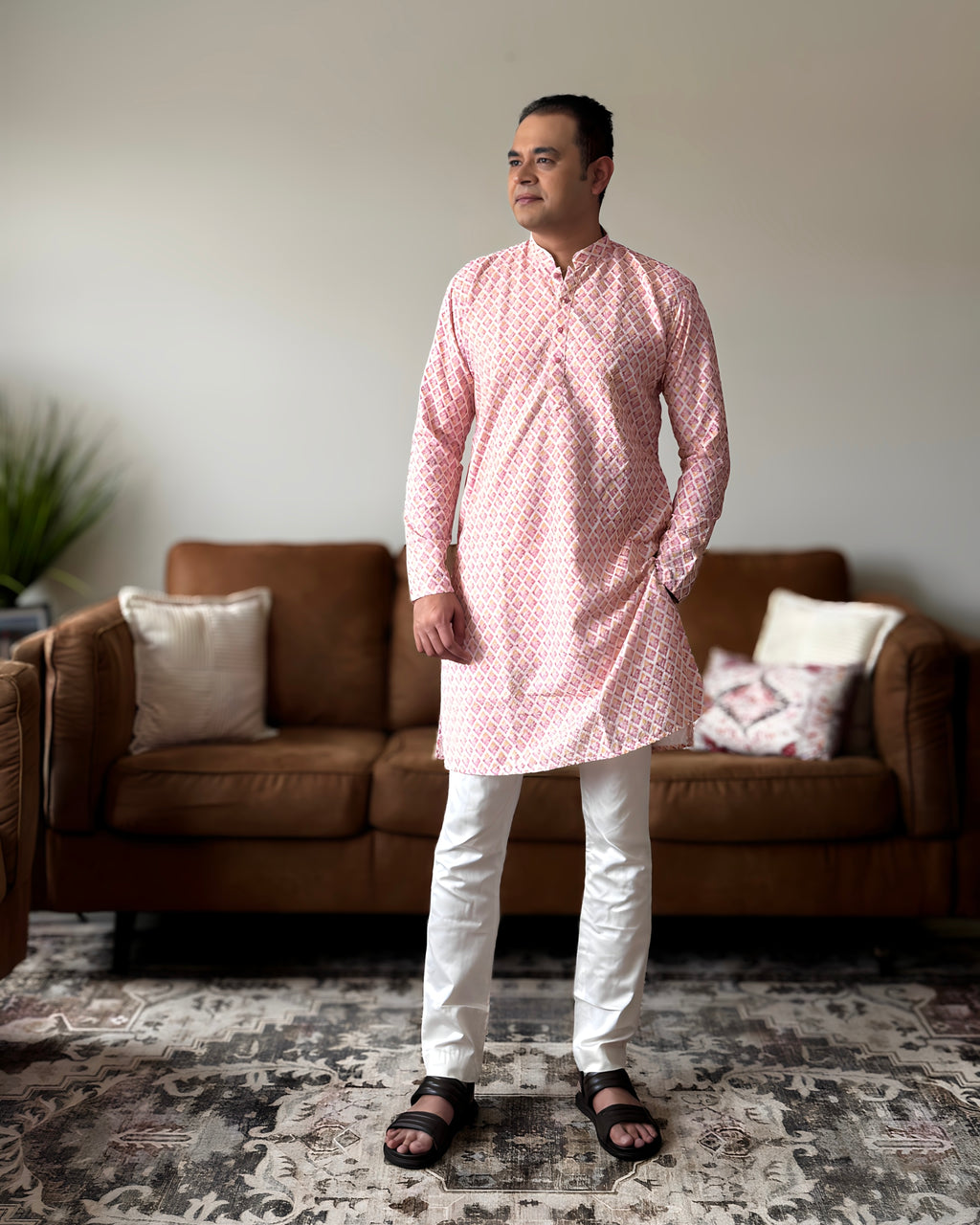Man wearing a pink kurta with white pants standing in a living room.