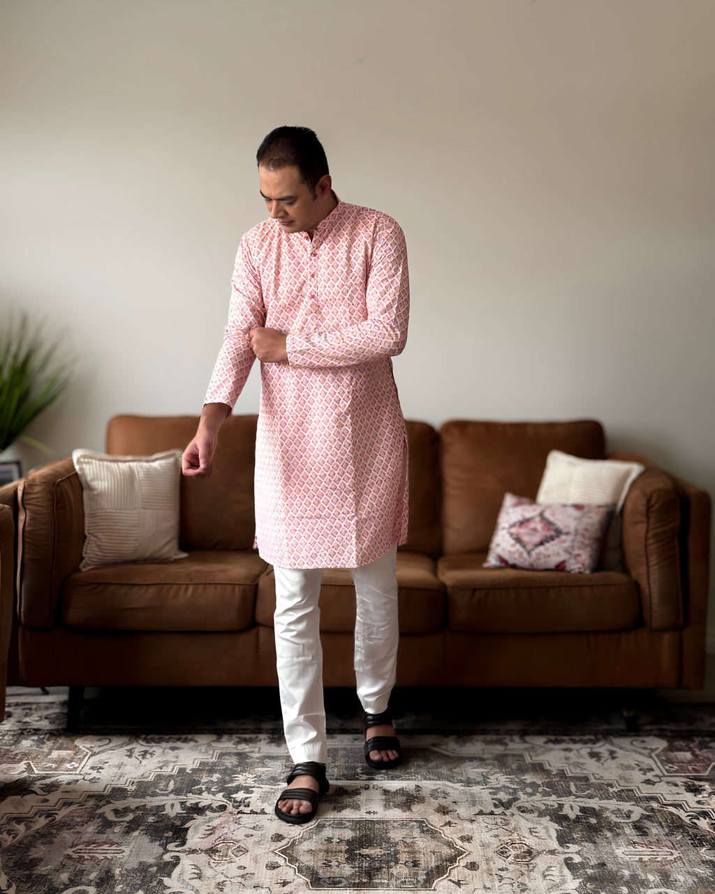 Man wearing a pink kurta with white pants standing in a living room.