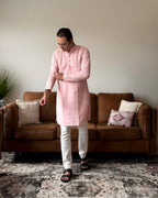 Man wearing a pink kurta with white pants standing in a living room.