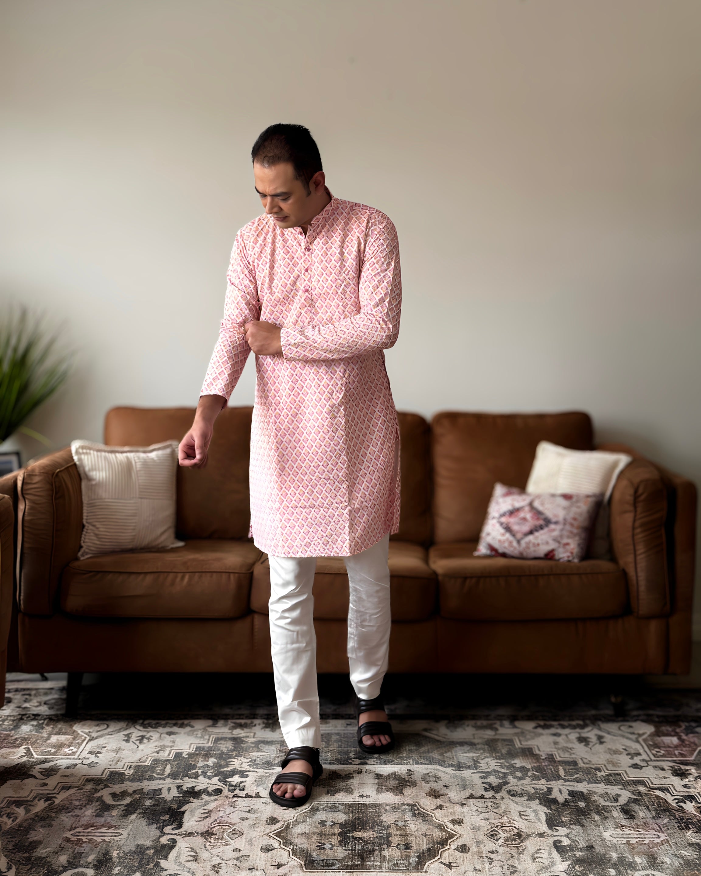 Man wearing a pink kurta with white pants standing in a living room.