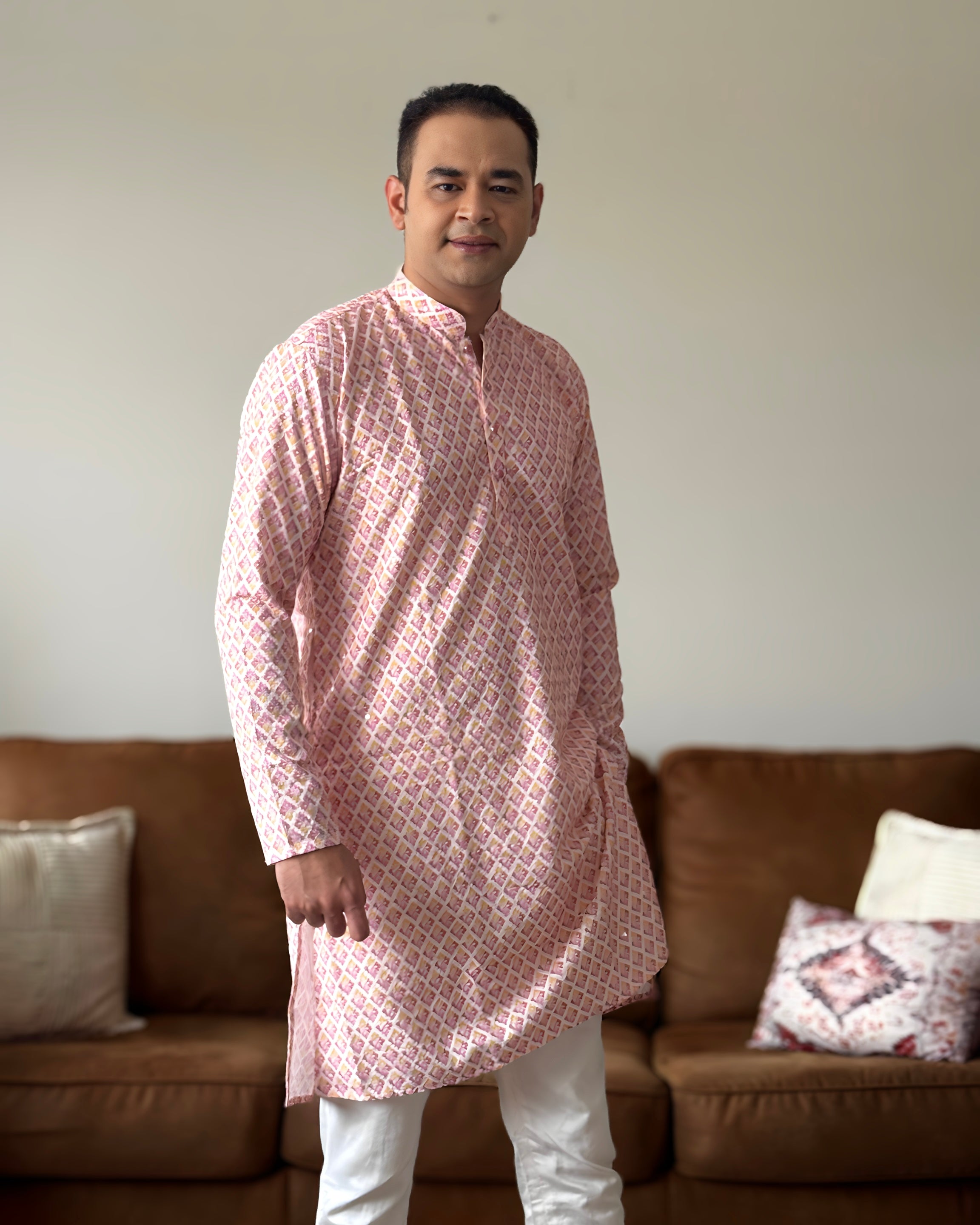 Man wearing a pink kurta with white pants standing in a living room.
