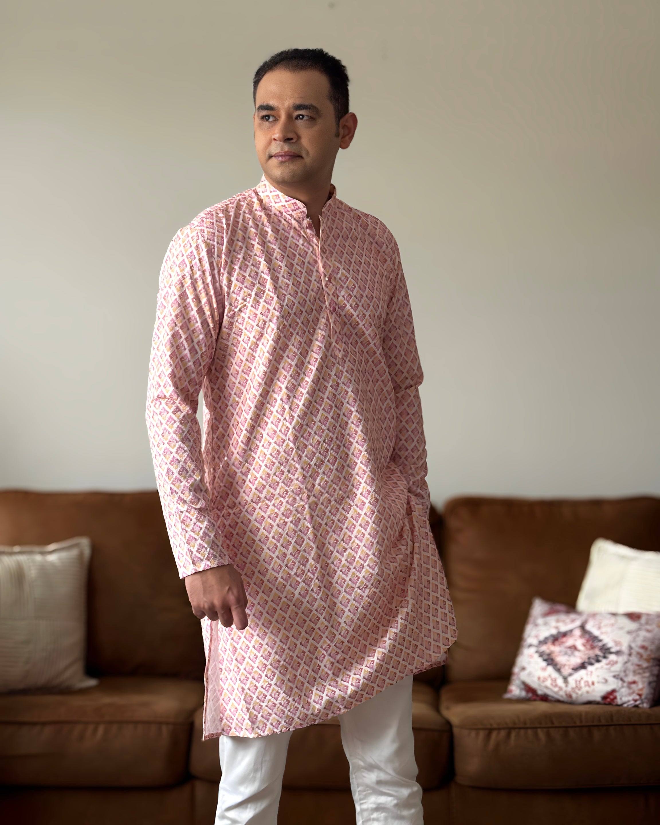 Man wearing a pink kurta with white pants standing in a living room.