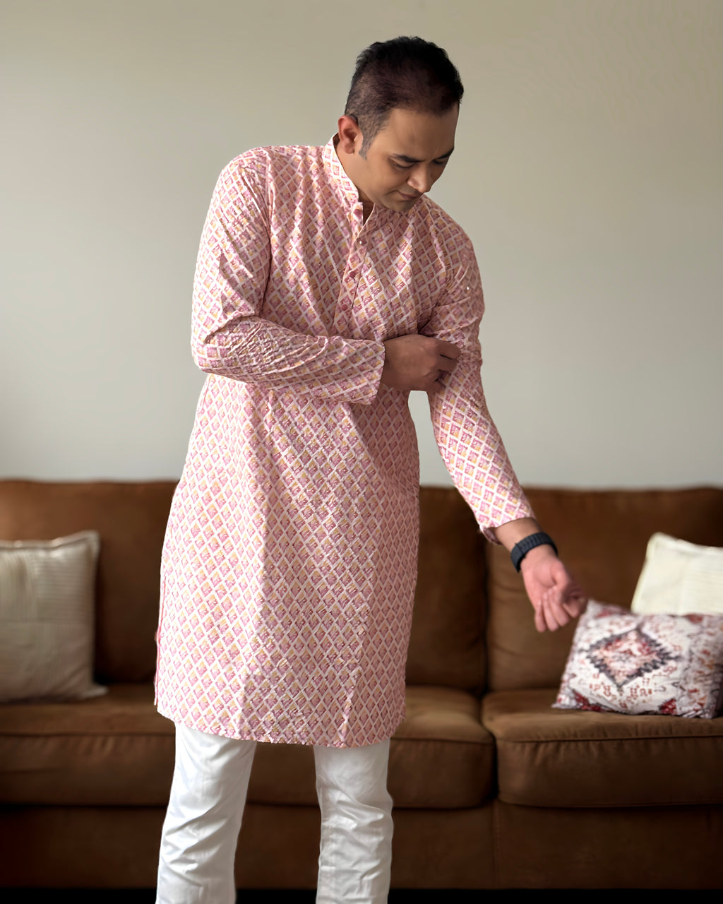 Man wearing a pink kurta with white pants in a living room setting.