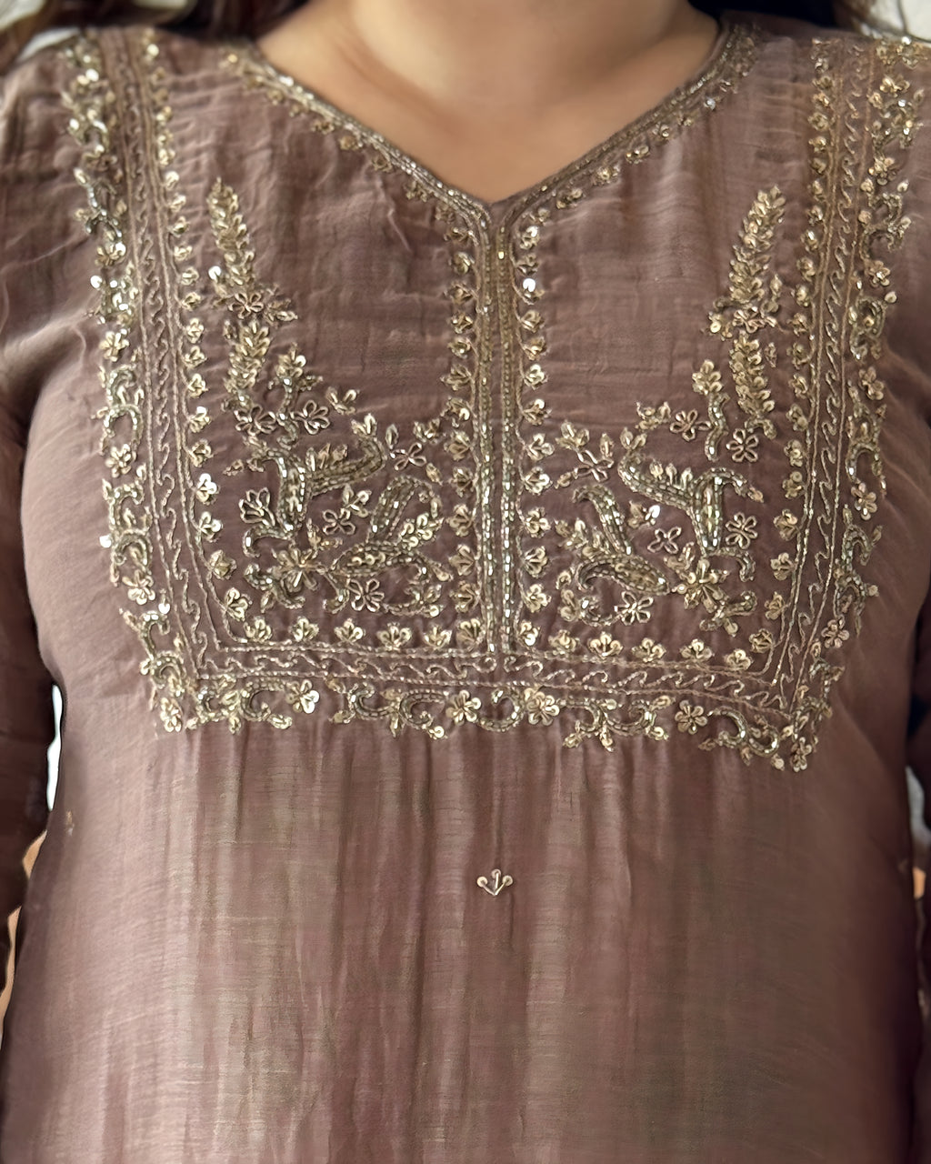 Close-up of a taupe-brown traditional tunic with ornate gold and silver embroidery around the V-neckline and chest panel.