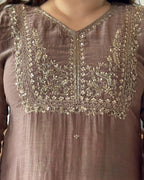 Close-up of a taupe-brown traditional tunic with ornate gold and silver embroidery around the V-neckline and chest panel.