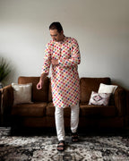 Man wearing a colorful patterned kurta standing in a living room.