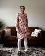 Man wearing a colorful checkered kurta standing in a living room.