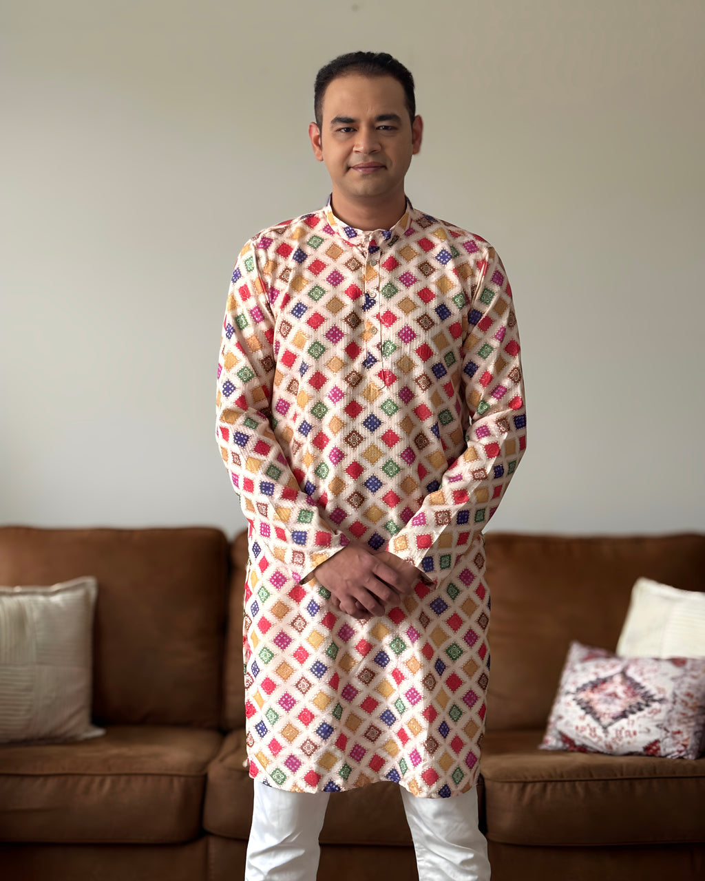 Man wearing a colorful patterned kurta standing in a living room.