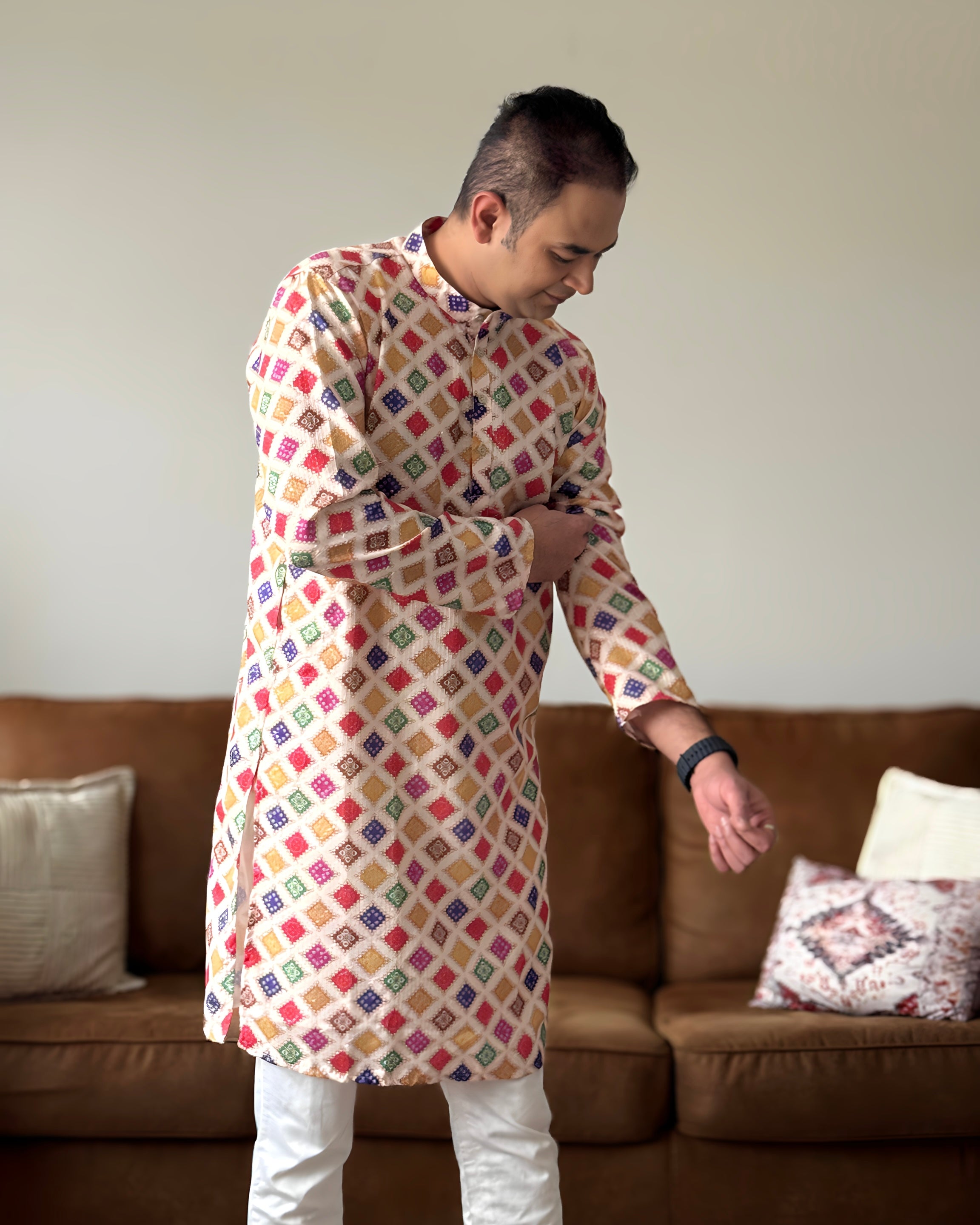 Person wearing a colorful patterned kurta standing in a living room.
