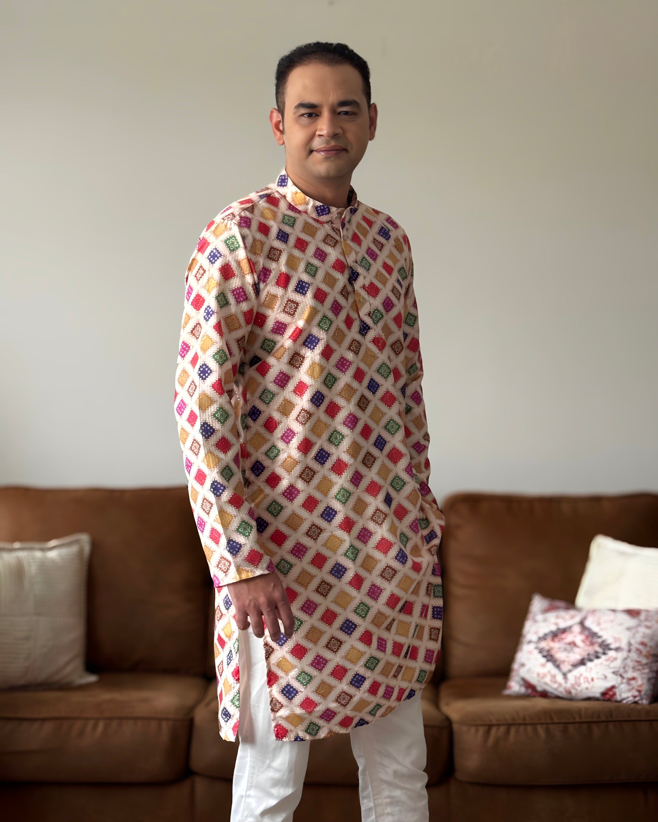 Man wearing a colorful patterned kurta standing in a living room.