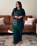 Woman wearing a green embroidered outfit standing in a living room.