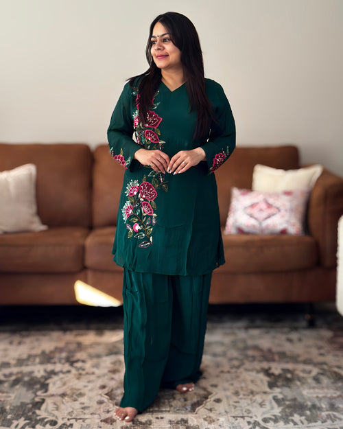 Woman wearing a green embroidered outfit standing in a living room.