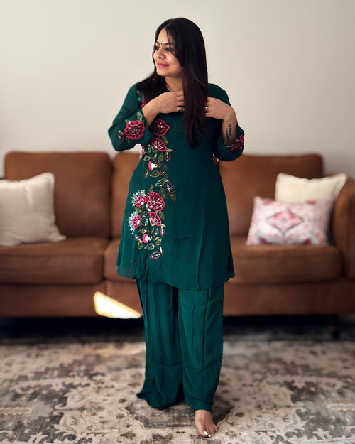 Woman wearing a green embroidered outfit standing in a living room.