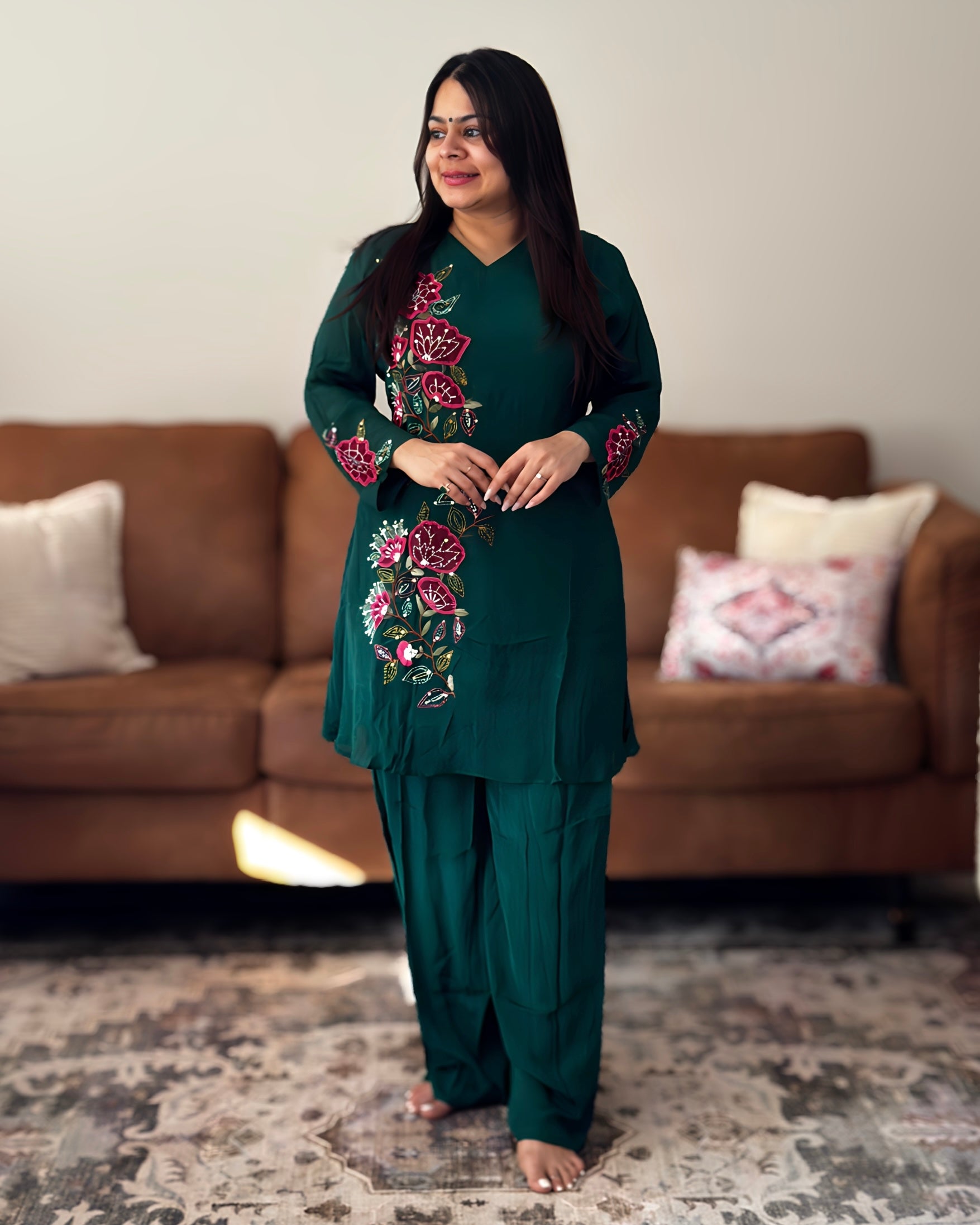 Woman wearing a green embroidered outfit standing in a living room.