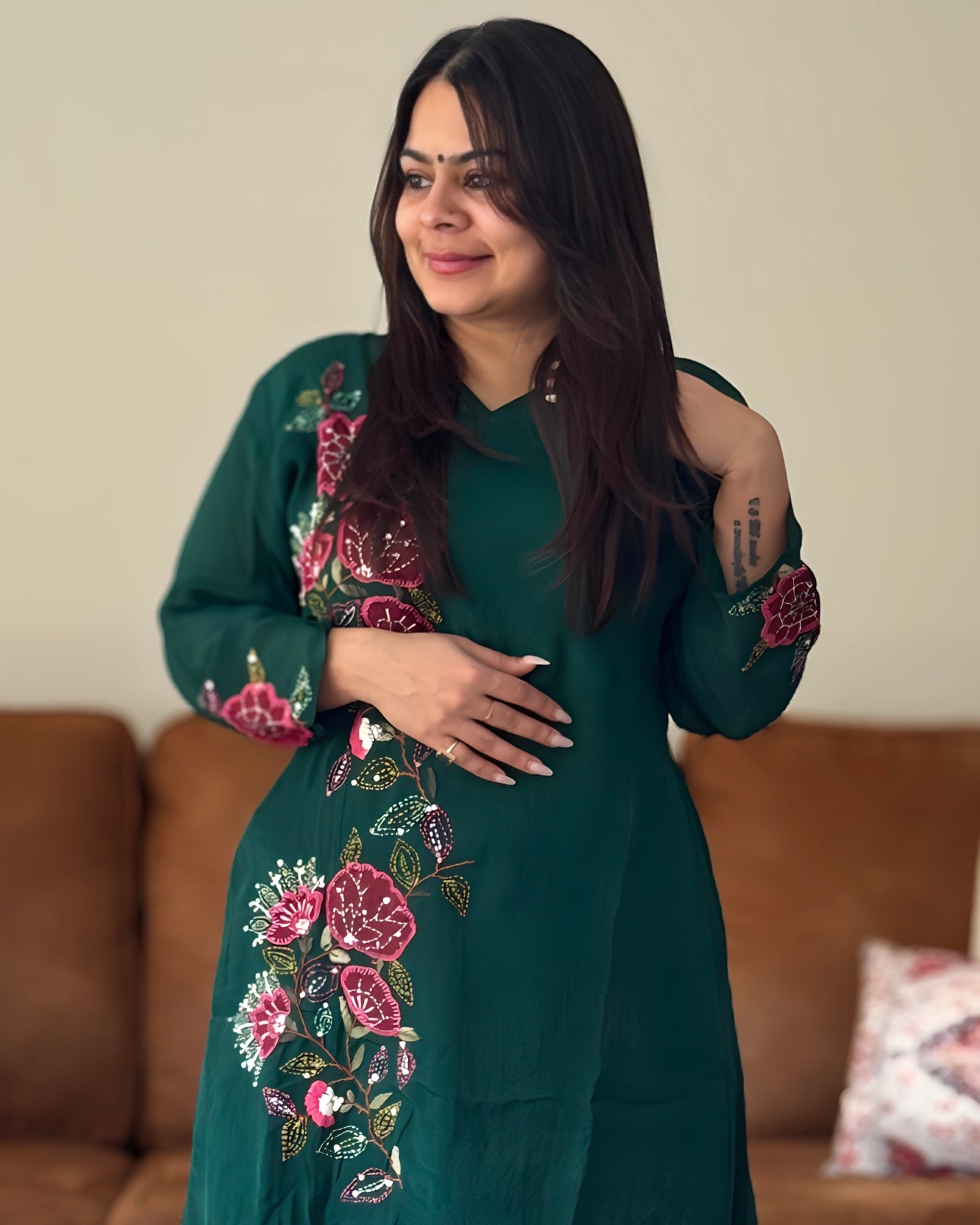 Woman wearing a green dress with floral embroidery in a living room setting