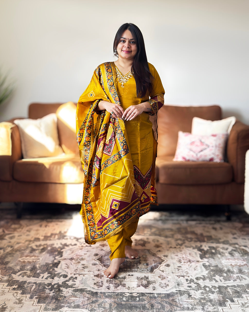 Woman in a yellow saree with a pattern standing in a living room.