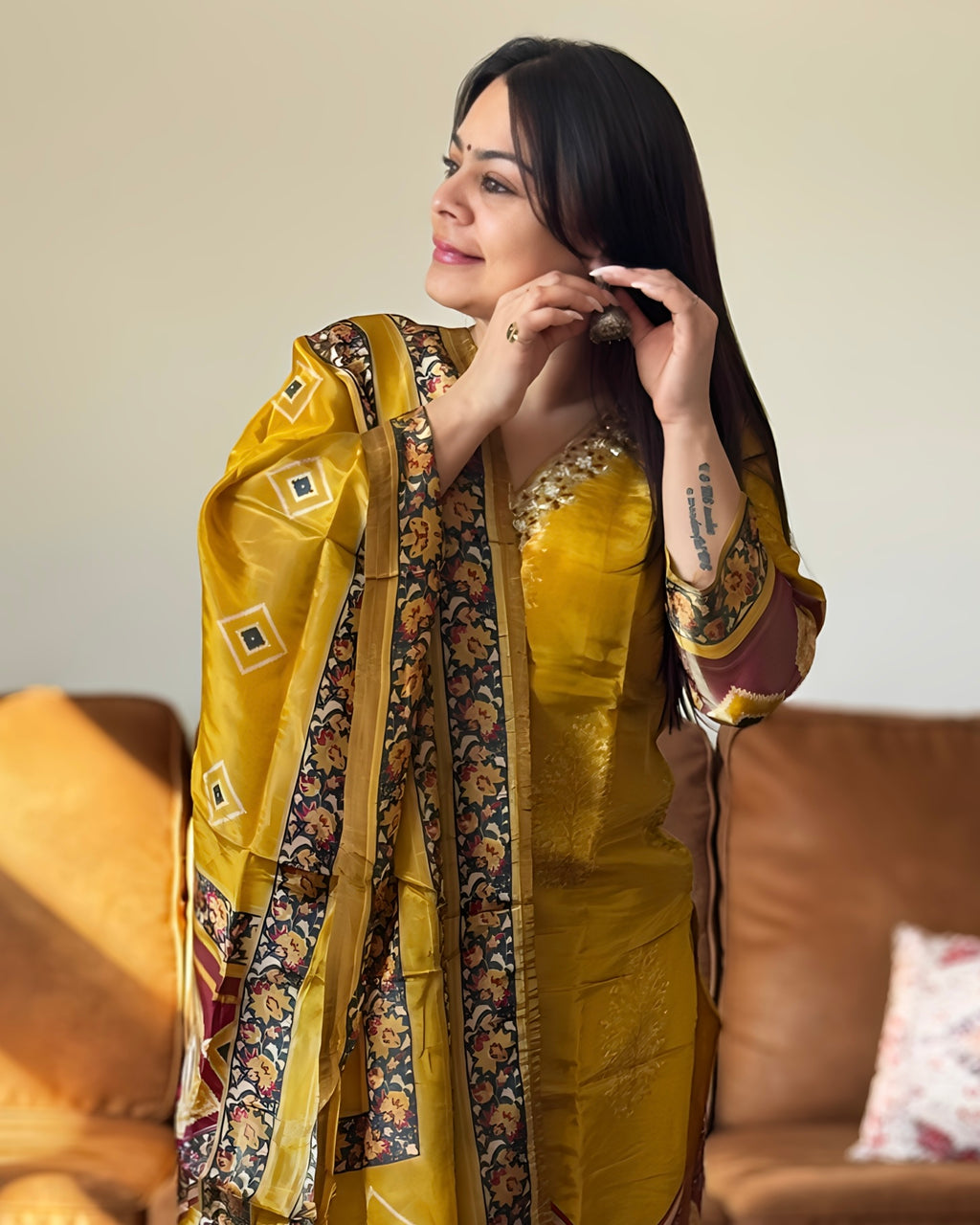 Woman wearing a yellow saree with a patterned border, sitting on a couch.