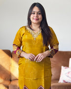 Woman wearing a yellow traditional outfit with intricate designs in a living room setting.