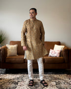 Man wearing a patterned kurta standing in a living room.