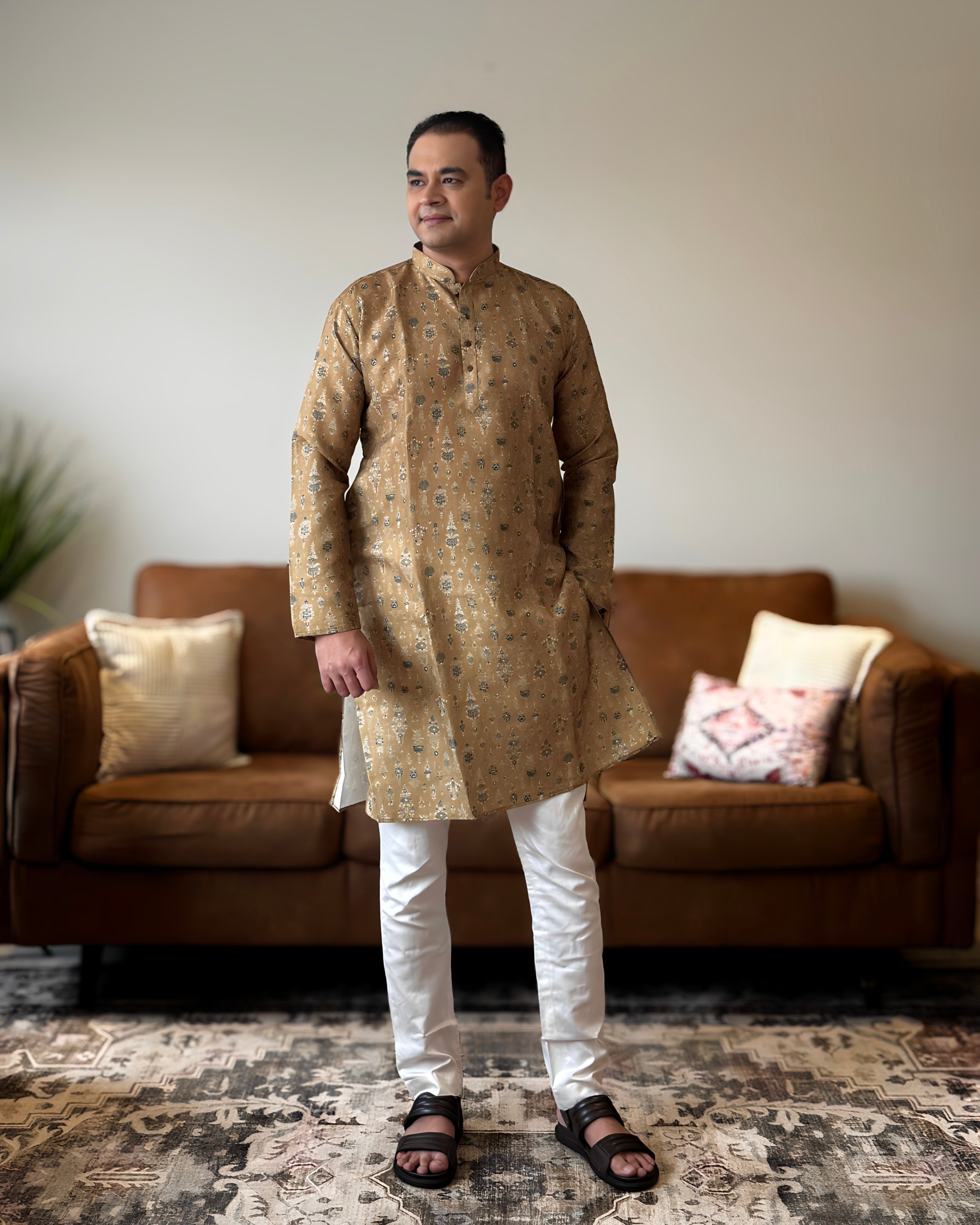 Man wearing a patterned kurta standing in a living room.