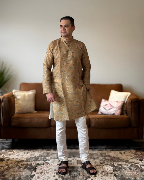 Man wearing a patterned kurta standing in a living room.