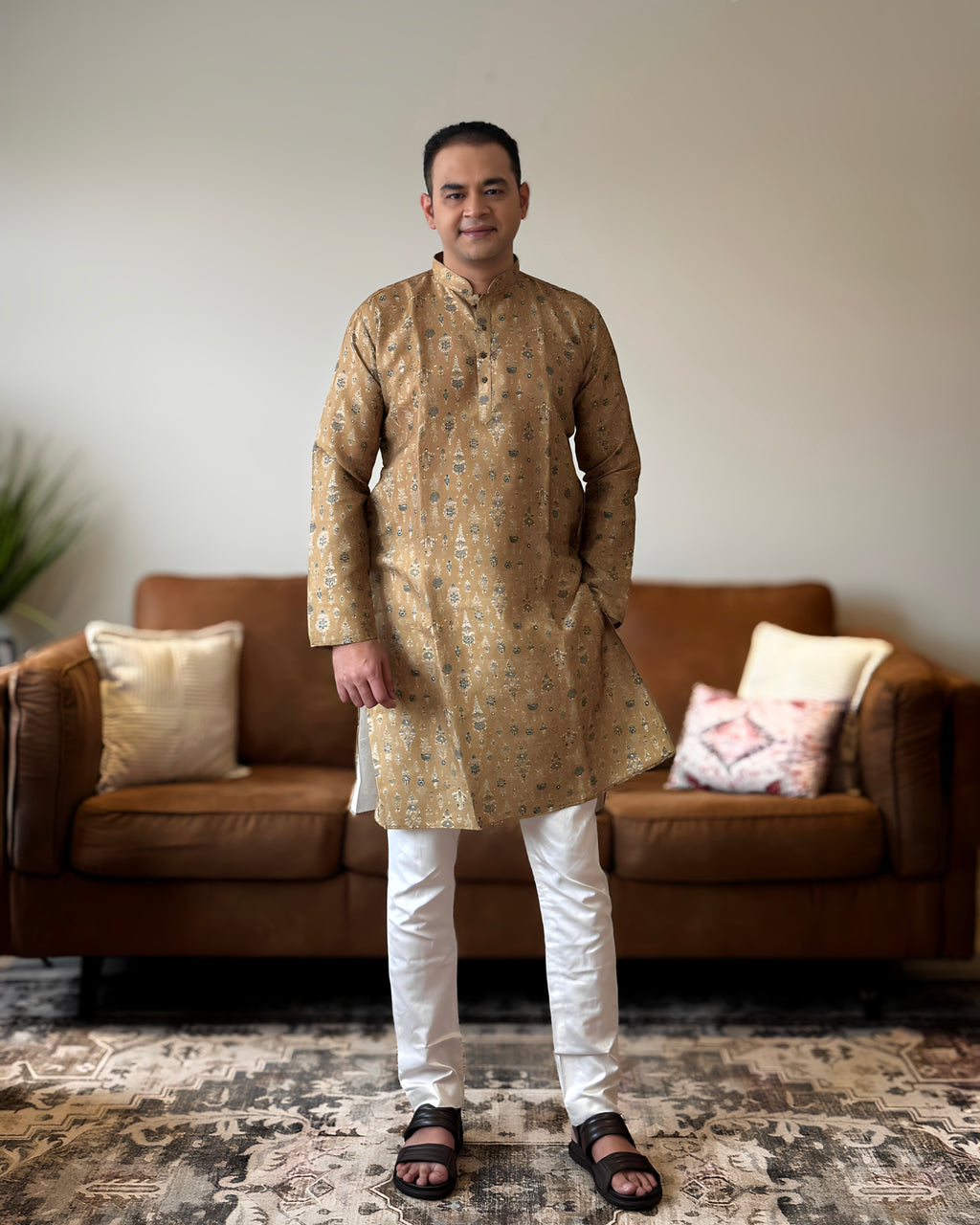 Man wearing a gold kurta with white pants standing in a living room.