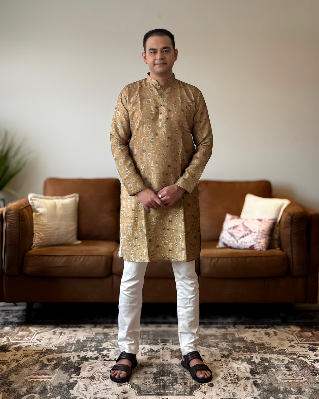 Man wearing a gold kurta with white pants standing in a living room.