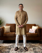 Man wearing a gold kurta with white pants standing in a living room.