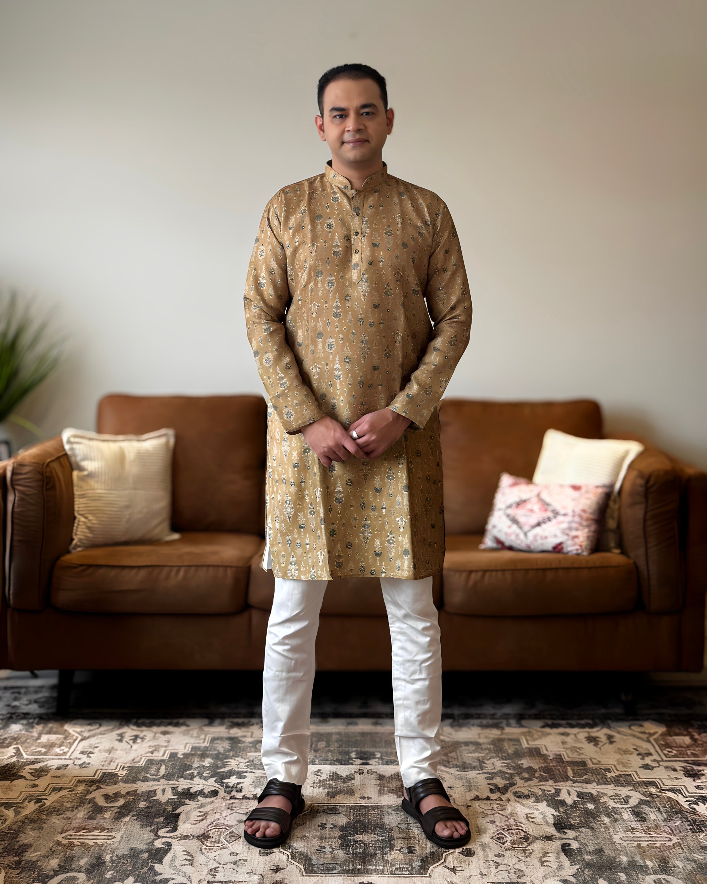 Man wearing a gold kurta with white pants standing in a living room.