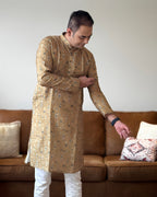 Man wearing a gold embroidered kurta in a living room setting