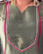 Close-up of a metallic olive green V-neck top with silver and pink embroidered neckline details, worn by a model with gold jewelry.
