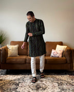 Man wearing a black and white kurta with white pants standing in a living room.