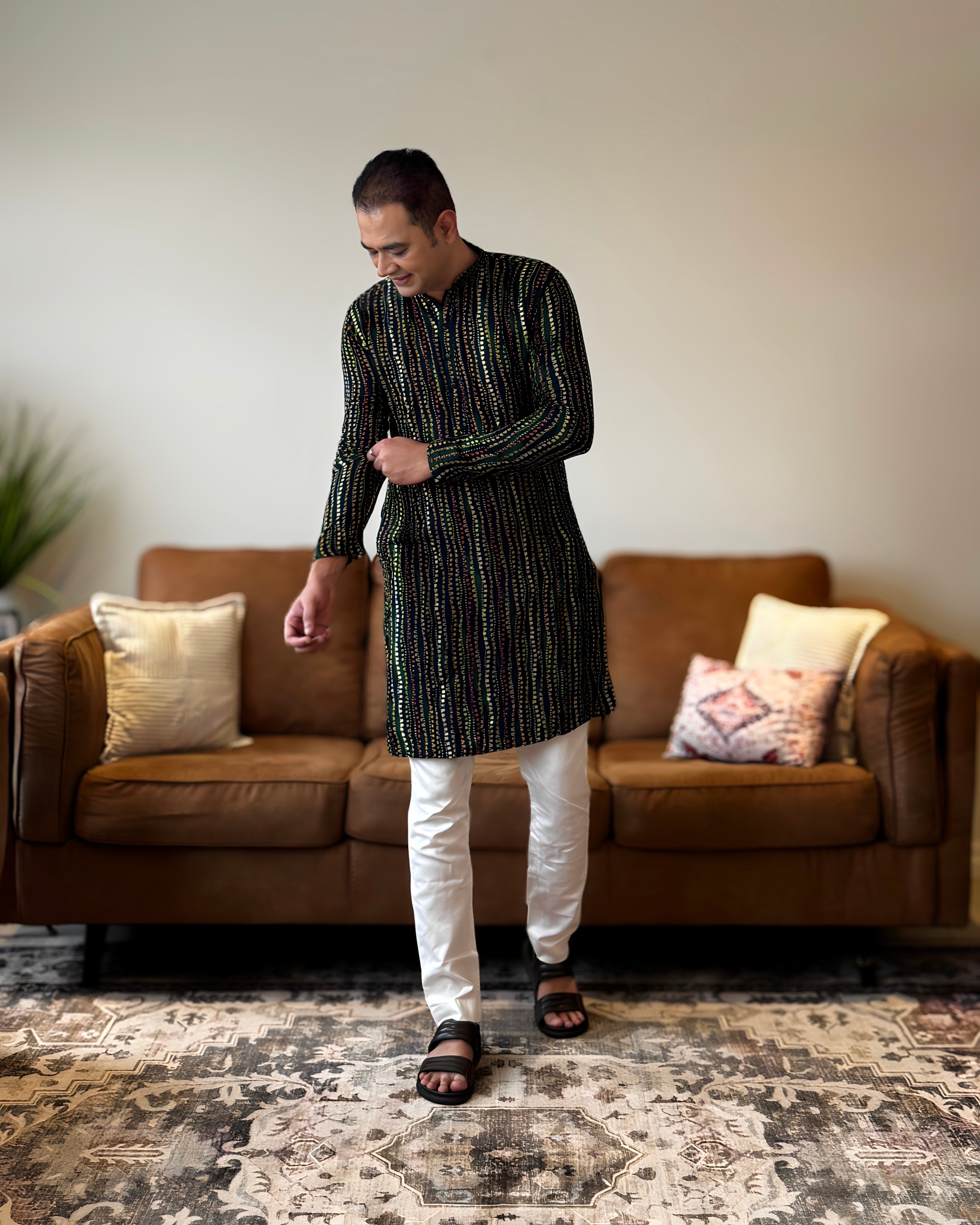 Man wearing a black and white kurta with white pants standing in a living room.