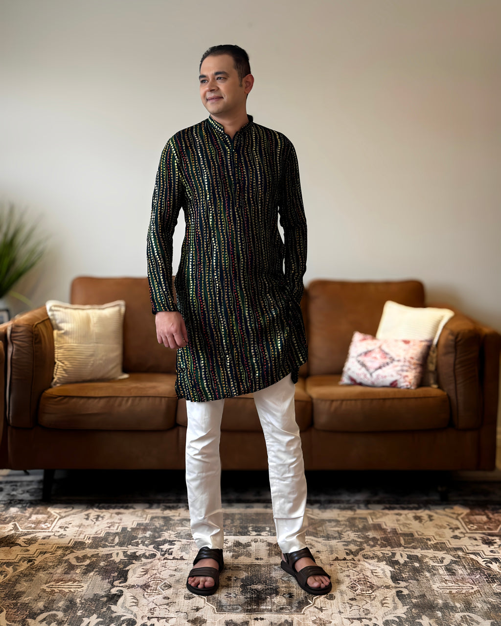 Man wearing a black and white patterned kurta with white pants standing in a living room.