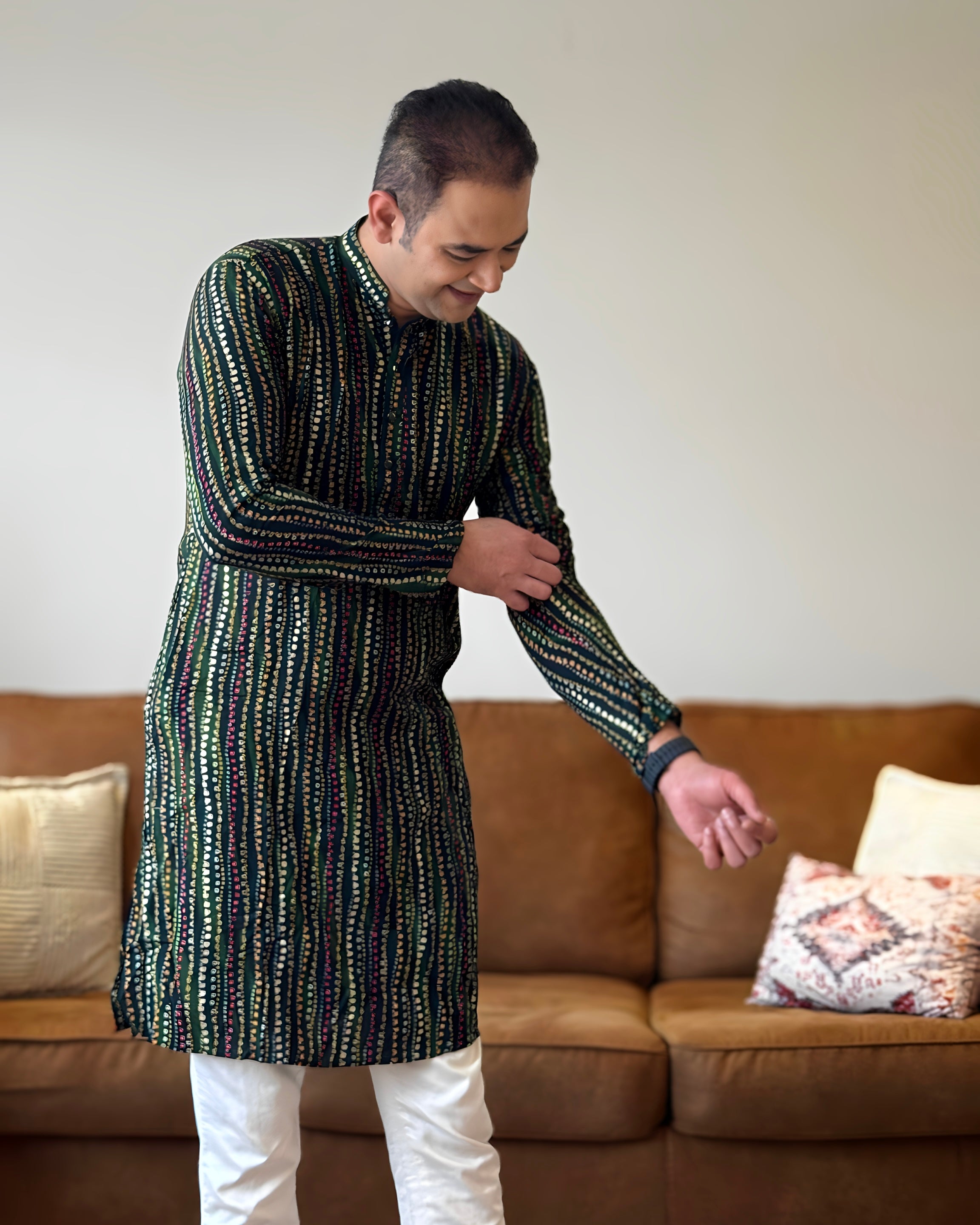 Man wearing a patterned kurta standing in a living room.