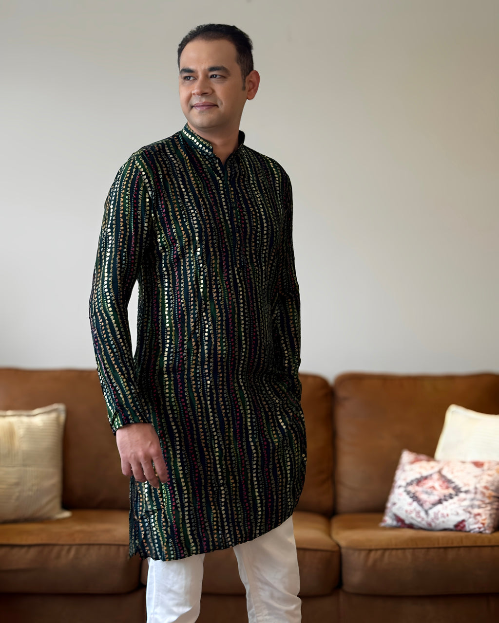 Man wearing a black kurta with white pants standing in a living room.
