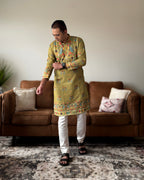 Man wearing a green kurta with white pants in a living room setting.