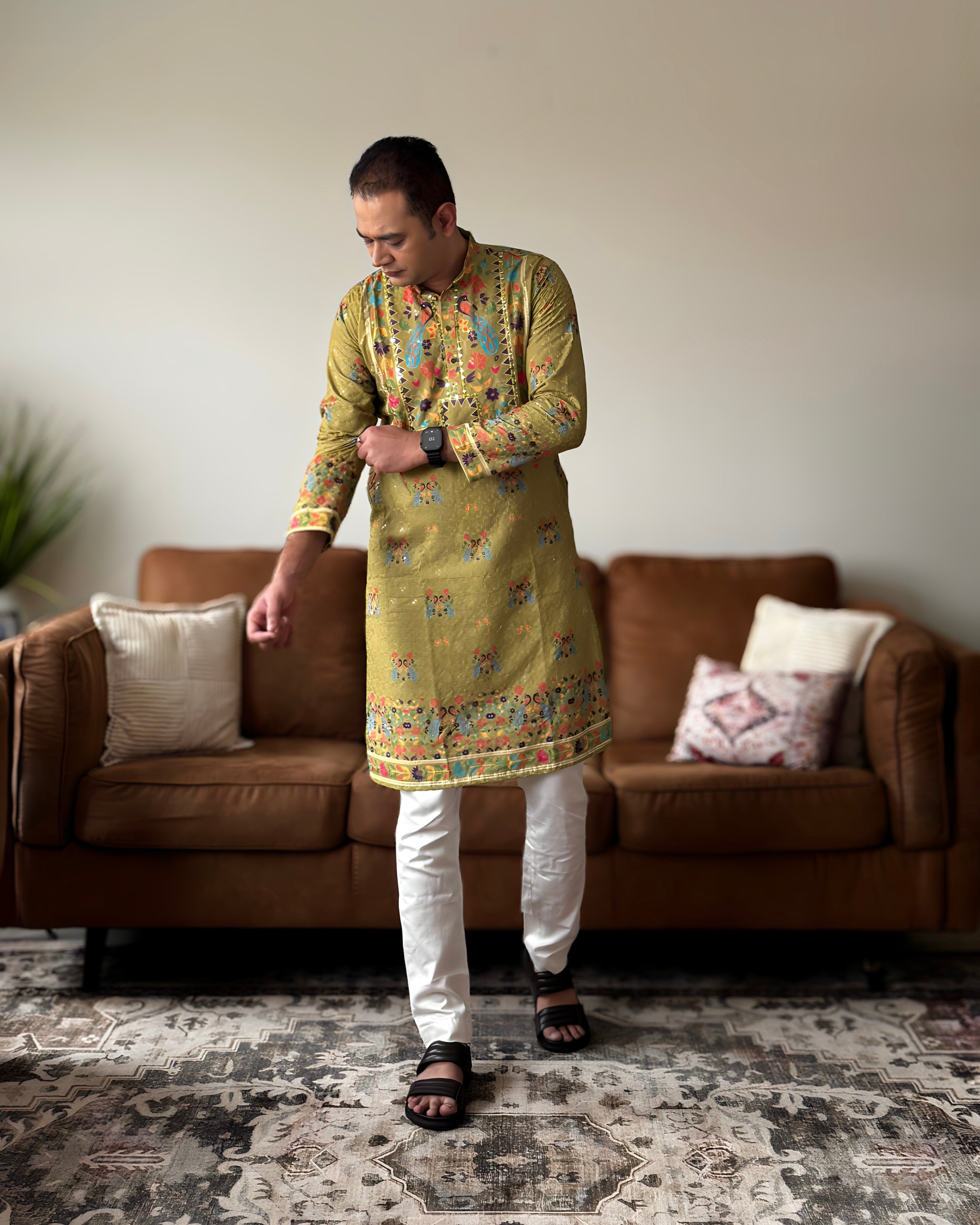 Man wearing a green kurta with white pants in a living room setting.