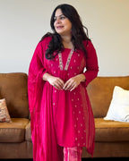 Woman wearing a bright pink traditional outfit with intricate designs, standing in a living room.
