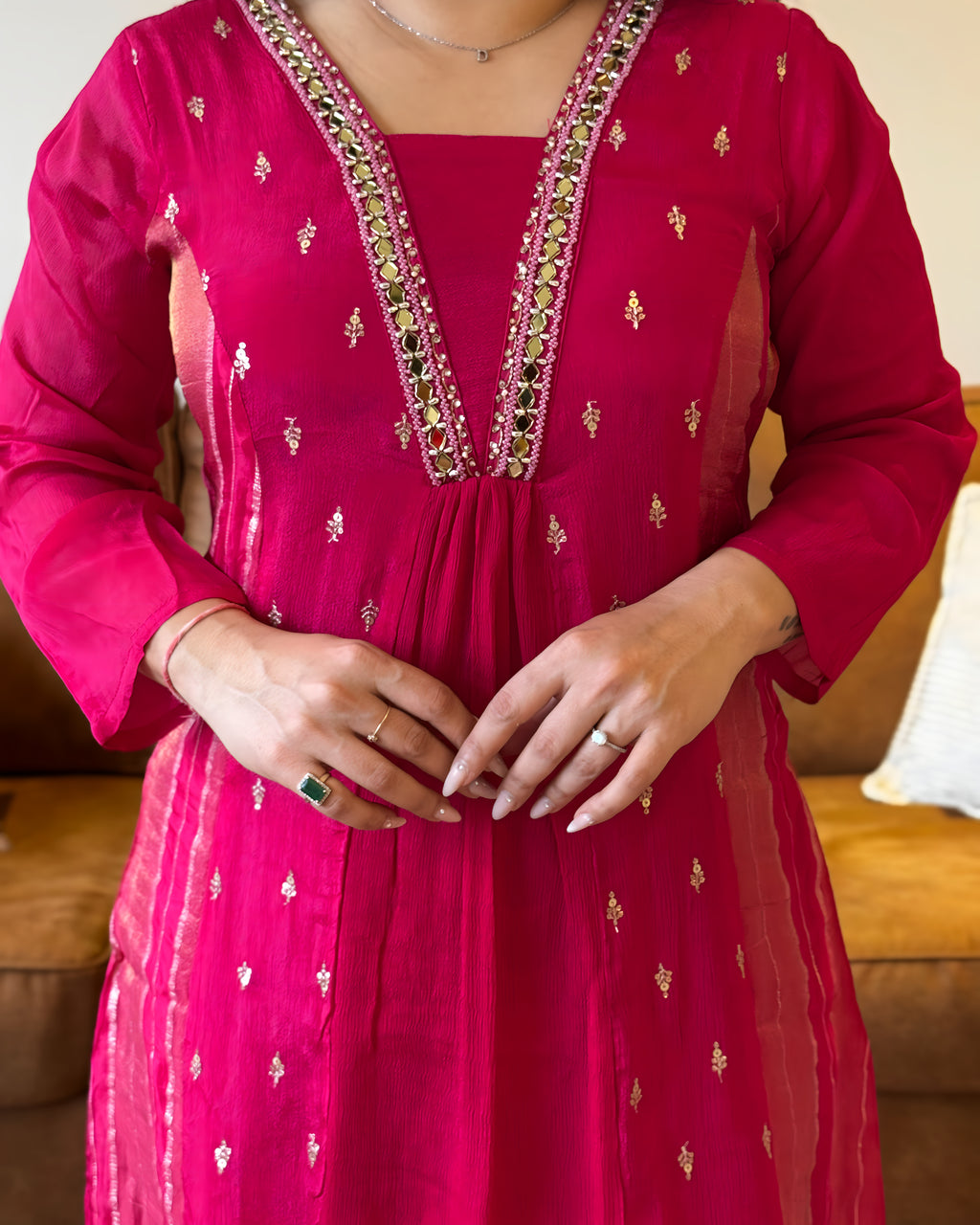 Person wearing a bright pink traditional outfit with intricate designs, sitting on a brown couch.
