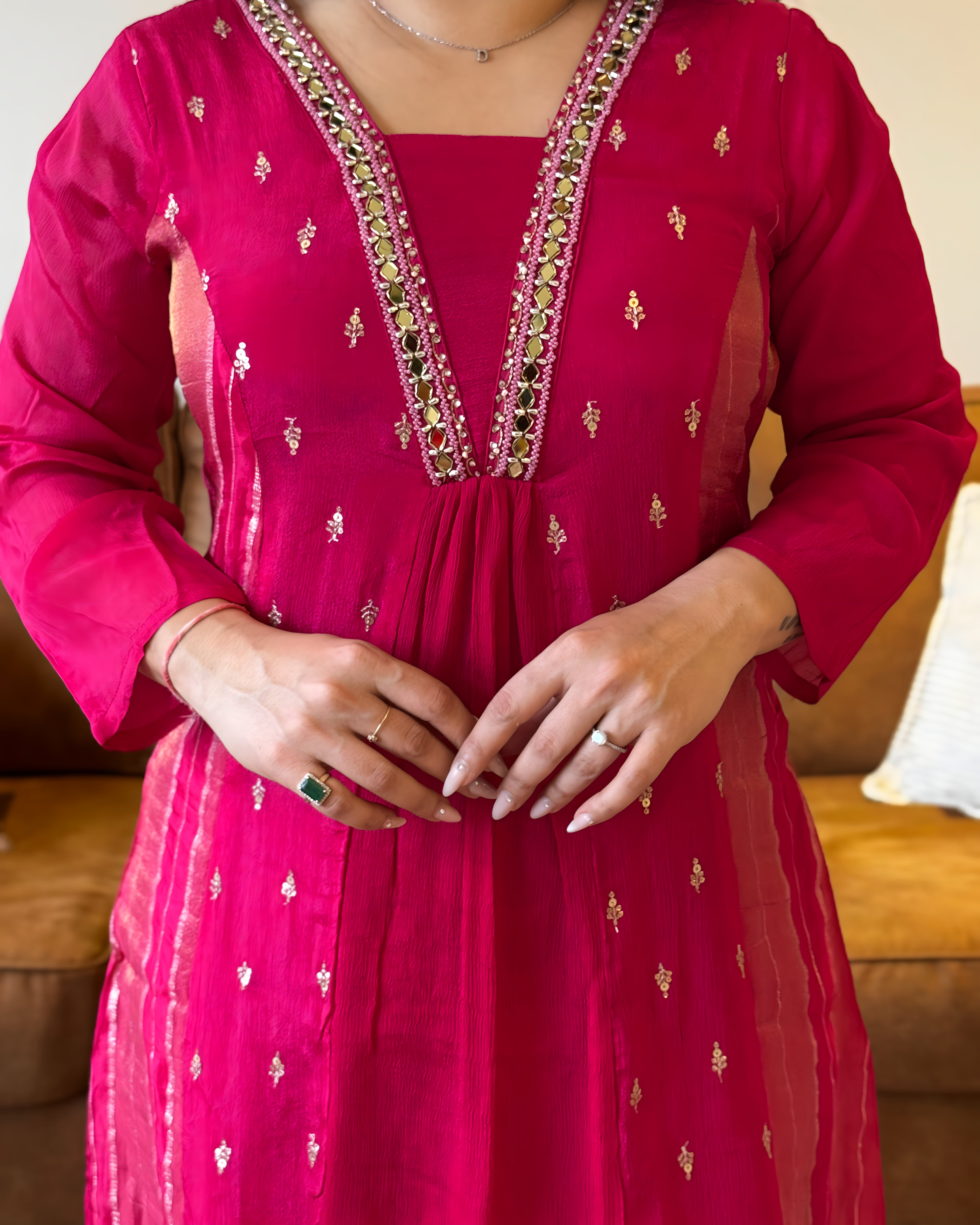Person wearing a bright pink traditional outfit with intricate designs, sitting on a brown couch.