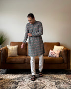 Man wearing a floral kurta and white pants standing in a living room.