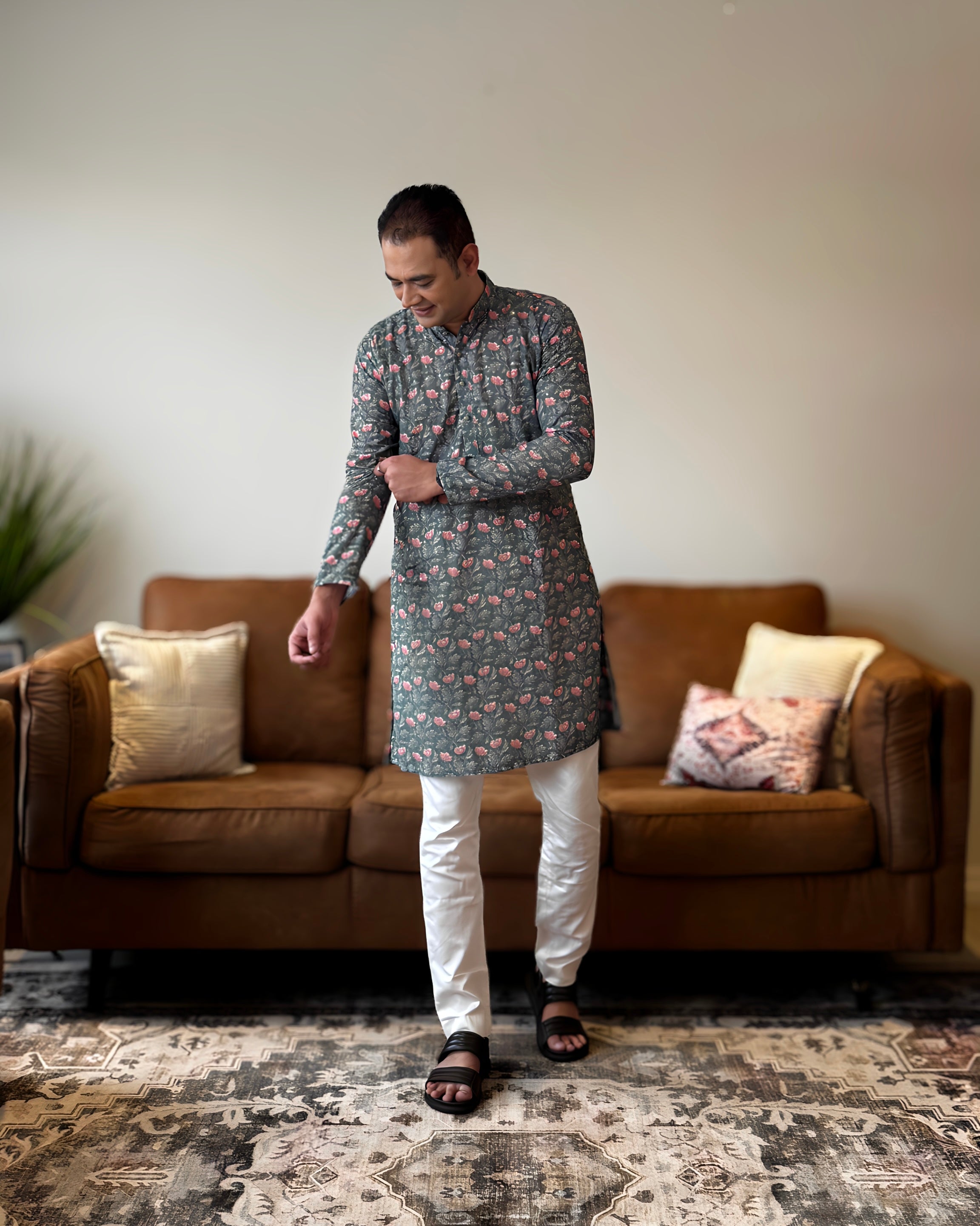 Man wearing a floral kurta and white pants standing in a living room.
