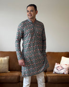 Man wearing a patterned kurta standing in a living room.
