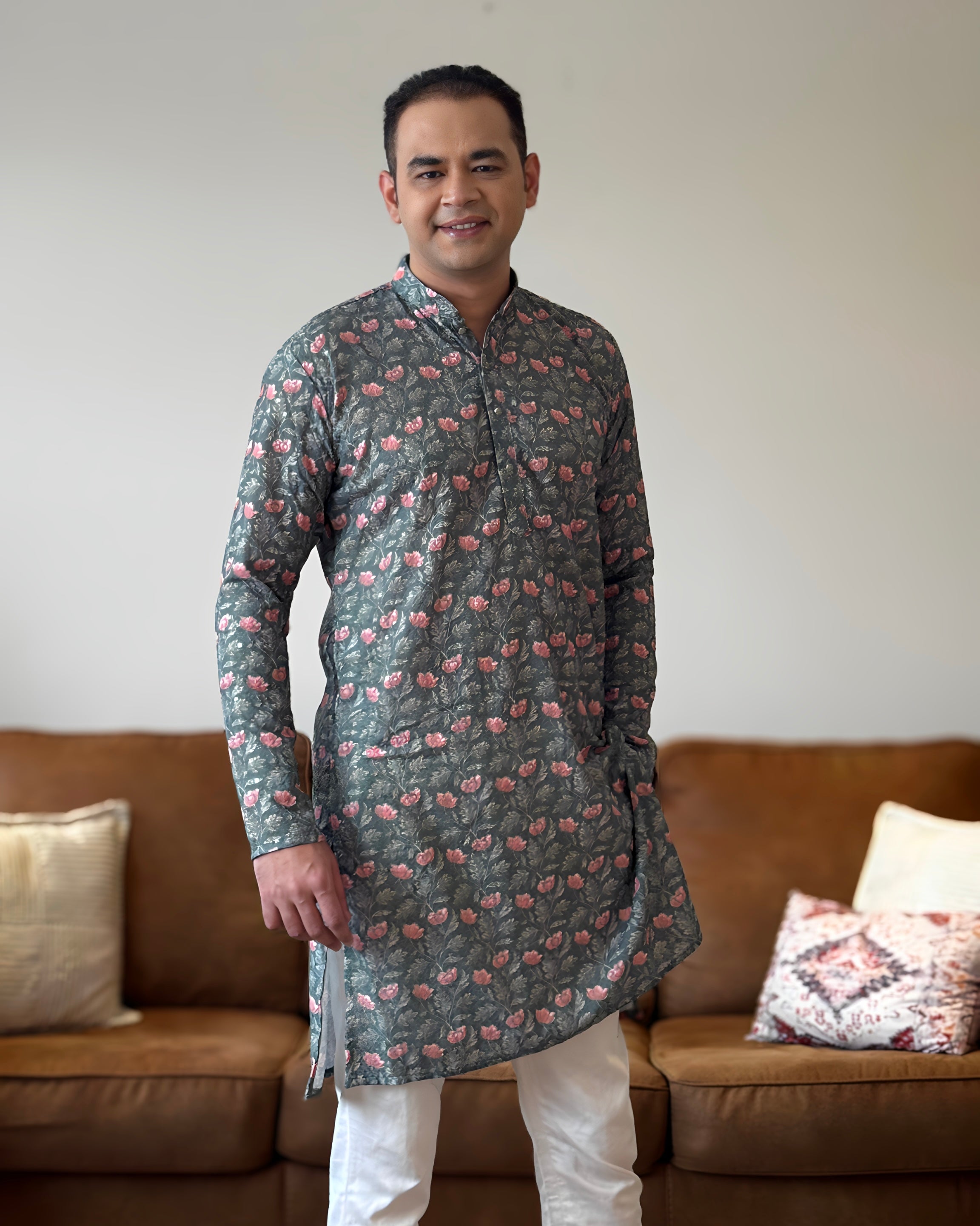 Man wearing a patterned kurta standing in a living room with a brown sofa and decorative pillows.